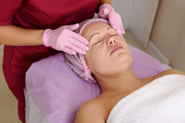 Fototapeta na wymiar Face peeling mask, spa beauty treatment, skincare. Woman getting facial care by beautician at spa salon