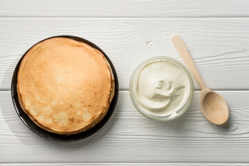 Flat lay composition with a plate of pancakes, sour cream and a wooden spoon on the table.