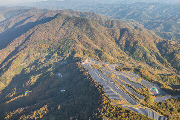 ソーラーパネルの傍を飛ぶパラグライダーと紅葉に染まる龍門山を空撮。和歌山県紀の川市