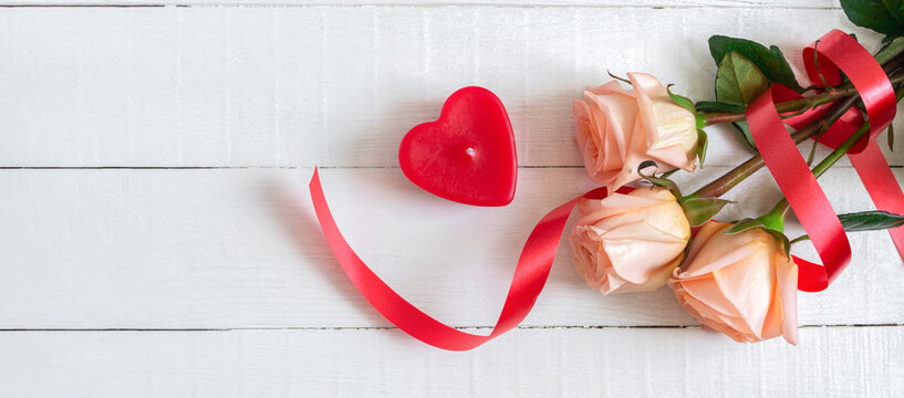 Bouquet of roses and a candle-heart on a white wooden background. The concept of wedding, valentine's day. Floral background with copy space. Top view.