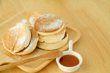 Fototapeta na wymiar Pancakes, sprinkle icing sugar in a wooden tray. Served with honey in a cup placed on a wooden table.