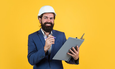 happy bearded man in hard hat at construction site with documents, architect