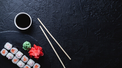 Sushi rolls with salmon, rice, eel and soy sauce on dark stone background, space for text, large banner