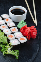 Sushi rolls with salmon, rice, eel and soy sauce on dark stone background