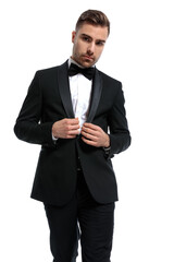 portrait of elegant fashion man buttoning black tuxedo