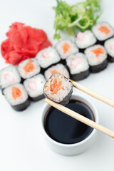 Bamboo sticks hold sushi rolls with salmon, rice and soy sauce in close-up