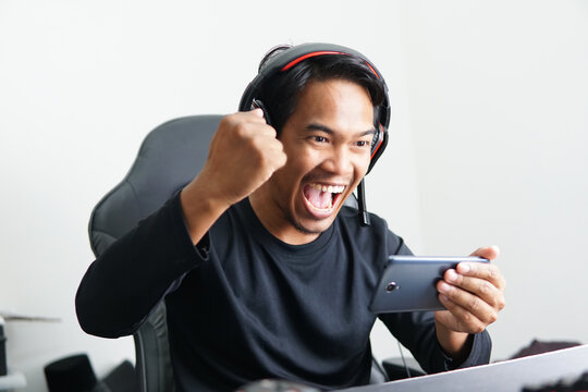Asian Gamer playing mobile game with excited expression emotion. Winning esport game