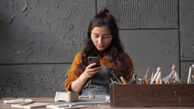 Young asian potter woman working on details of a clay handcraft piece. Work with different pottery tools. Concept of creative leisure time and ceramics. Start up small business, artwork and interior