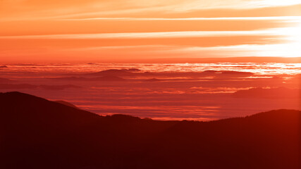 The sun's rays illuminate the mountain tops and the fog at dawn.
