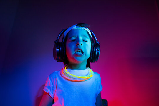 Cyberpunk Boy Child In A White T Shirt And Large Headphones Listening To Music On The Background Of The Wall