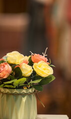 Artificial bouquet in vase, yellow and coral pink roses on bokeh background, decorative bouquet concept