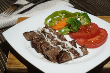 Closeup of sliced grilled steak with tomatoes and broccoli on a white porcelain plate