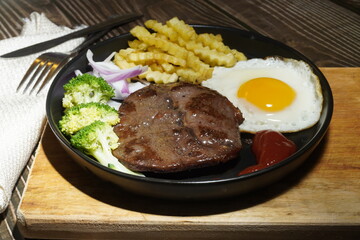 Closeup of grilled steak and fried egg in black plate on wooden board, homemade cuisine