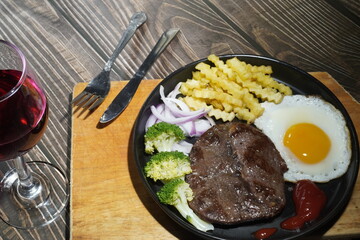 Grilled steak with fried egg. Fork, knife and red wine on wooden table, top view