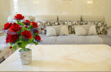 A pot of red artificial roses on the table and sofa in the living room, stylish and simple modern room
