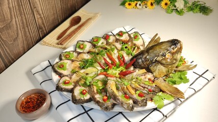 Close-up of a plate of steamed fish garnished with red chili on the table, top view, homemade food
