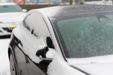 black parked car covered with thick layer of ice and snow in the street in Boskoop, the Netherlands