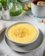 Corn porridge in a ceramic plate on the light gray kitchen table. Porridge of polenta with spices. Cream soup of polenta. Healthy Vegetarian breakfast