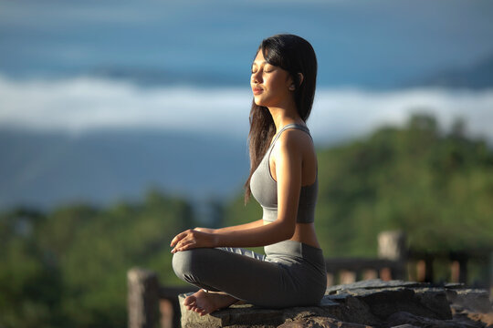 Beautiful young asian woman siting in lotus position meditates on top of mountain in in a Natural National Park of Philippines. Healthy lifestyle outdoors at sunrise. Travel Asia concept. High
