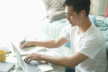 Obraz premium asian young student man entrepreneur wear earphones working with computer studying learning online at home. e-learning webinar meeting. social distance in covid pandemic
