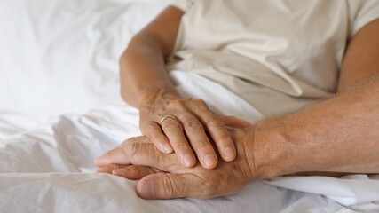 An old man puts his hand on old womans hand lying in bed. 