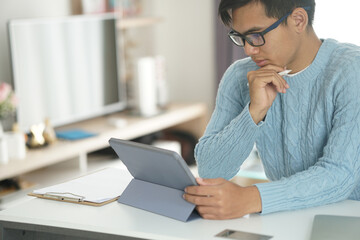 Fototapeta premium asian young student man entrepreneur working with tablet studying learning online at home. e-learning webinar meeting. social distance in covid pandemic