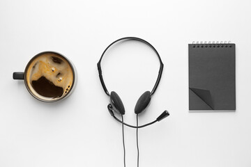 Headset with notebook and cup of coffee on white background