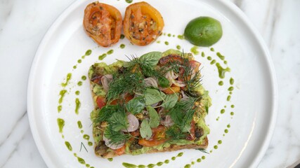 Top view of plant based toast with avocado smash topped with lots of vegetables
