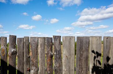 Old wooden fence against a blue sky with clouds on a sunny day