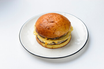 Giant perfect burger with ham and cheese served on a clear white plate over plain white background.