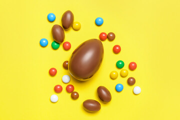 Tasty chocolate eggs and candies on color background