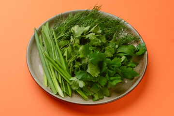 Fresh herbs - onion, dill and parsley on a plate over orange background. Healthy fresh greenery,