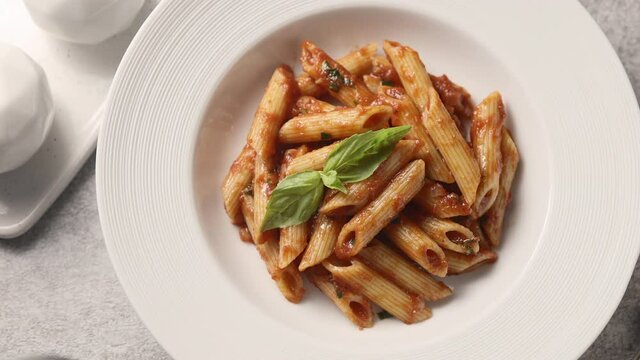 Penne pasta with tomato sauce and basil in a plate, light background, the camera moves along, close-up 