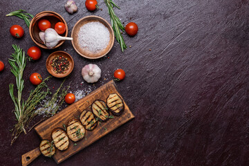 Tasty grilled eggplant with spices and vegetables on dark background