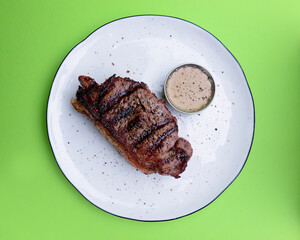 Delicious beef steak with sauce served on a white plate over bright green background. BBQ meat, barbecue concept.