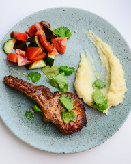 Barbecue Tomahawk Steak with mashed potatoes and vegetables. Served on a blue plate over white...