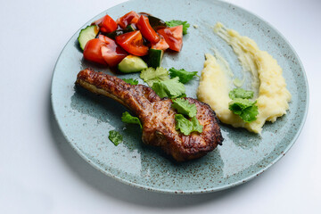 Barbecue Tomahawk Steak with mashed potatoes and vegetables. Served on a blue plate over white background.