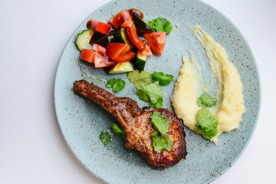 Barbecue Tomahawk Steak with mashed potatoes and vegetables. Served on a blue plate over white background.