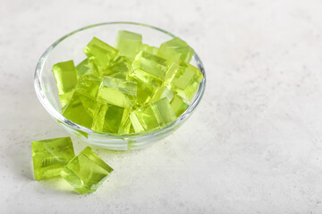 Glass bowl with tasty jelly cubes on light background