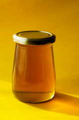 Natural sugar substitute, healthy food concept. Raw bee honey in glass jar on yellow background.