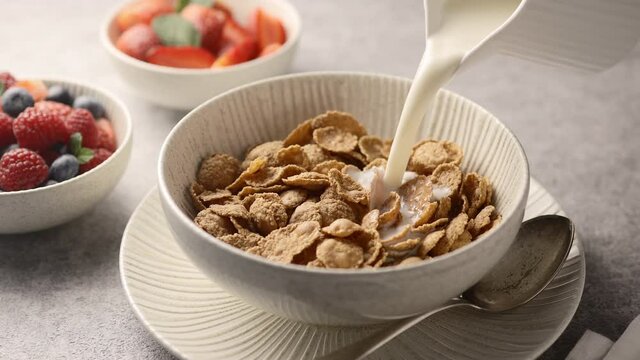 The girl pours milk into the breakfast cereal. On the background of berries, close-up 