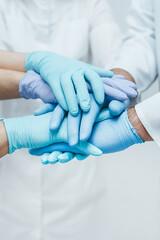 Team of medical workers in blue gloves holding hands together. Closeup.