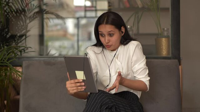 Happy young woman holding phone looking at screen waving hand on video call with long distanced friends,relatives using video calling apps on her notepad.pleasant video call talk concept in office