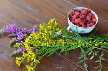 Freshly picked raspberries in a beautiful cup and a bouquet of wild flowers on a wooden table