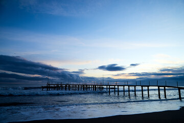 Obraz premium View from beach to water of sea, waves with white foam, pierce and sky with clouds in a nice evening.