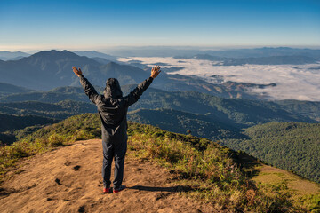 Man hiking raise hand enjoy succeed and looking at mountain range on the top of mountain in tropical forest, Outdoor adventure travel concept