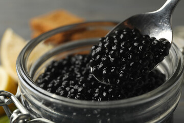 Fototapeta na wymiar Glass jar and spoon with black caviar, close up