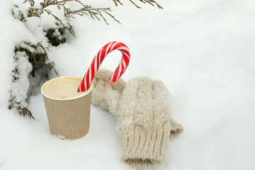 Obraz na płótnie Canvas Paper cup with coffee and candy canes and mittens outdoor in winter
