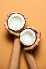 Fot the best drink. Top view of female hands holding halves of coconut isolated over orange...