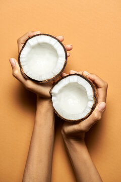 Fot the best drink. Top view of female hands holding halves of coconut isolated over orange background. Healthy eating concept